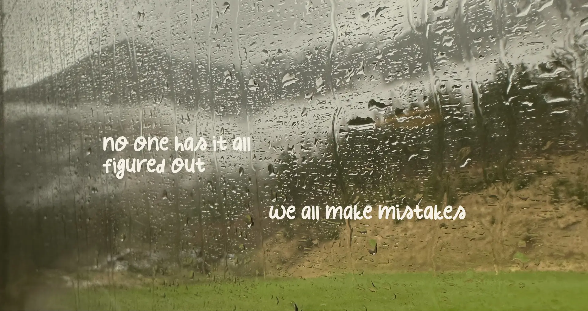 Scenery of the mountain and field outside, from the train window, with rain droplets running down.